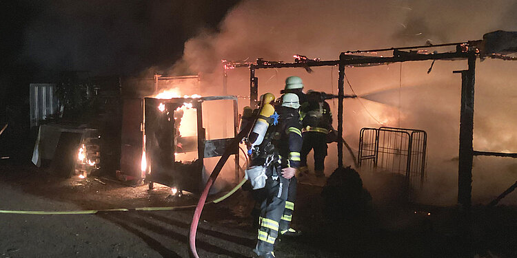 Feuerwehrleute löschen nachts einen brennenden Carport
